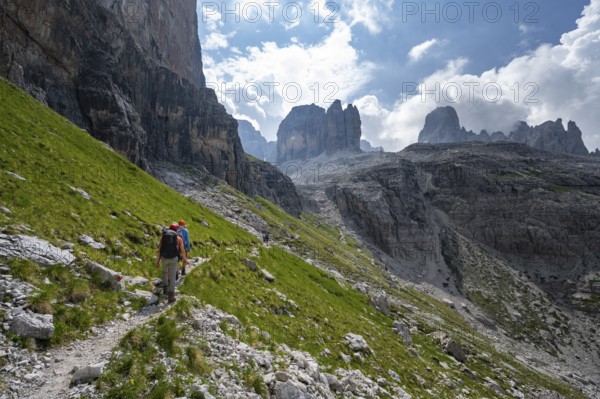 Two mountaineers on a hiking trail in front of a picturesque mountain landscape with rocky peaks,