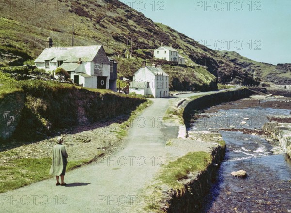 Road passing historic buildings by harbour wall fishing village of Boscastle, Cornwall, England, UK