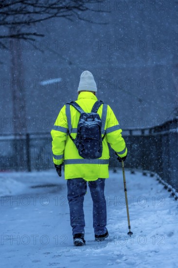 Winter weather, blowing snow, man walking on a snowy sidewalk with a walking stick, North