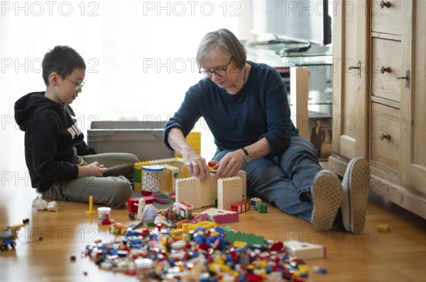 Elderly woman, grandma, boy, 6 years, grandson, glasses, multi-ethnic, playing together with Lego,