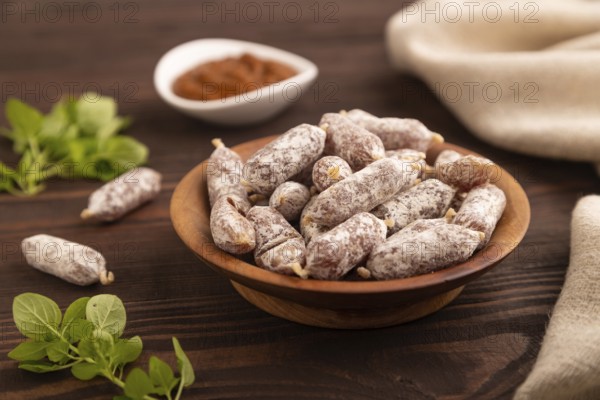 Small smoked Chicken sausages in wooden bowl on brown wooden background and linen textile. side