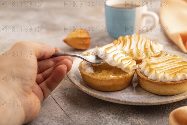 French lemon tart with meringue with hand on brown concrete background, cup of coffee, orange linen