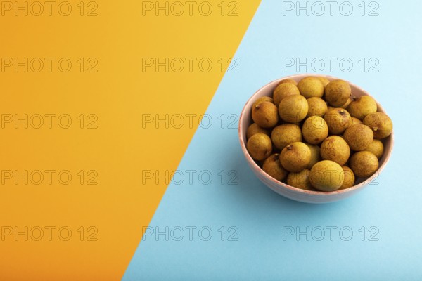 Ripe Longan in ceramic bowl on blue and orange pastel paper background, side view, copy space,