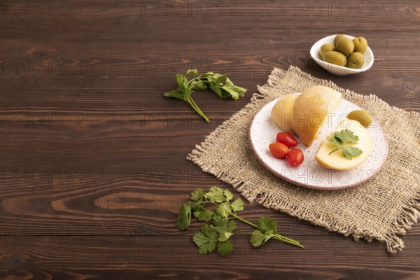 Smoked Mozzarella cheese, with tomatoes and olives on brown wooden background and linen textile,
