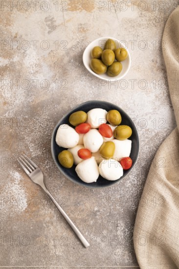 White Mozzarella cheese, with tomatoes and olives in blue bowl on brown concrete background and