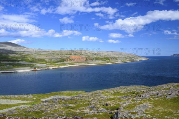 Green meadows on the banks of Syltefjord with clouds in the blue sky, landscape with a lake and