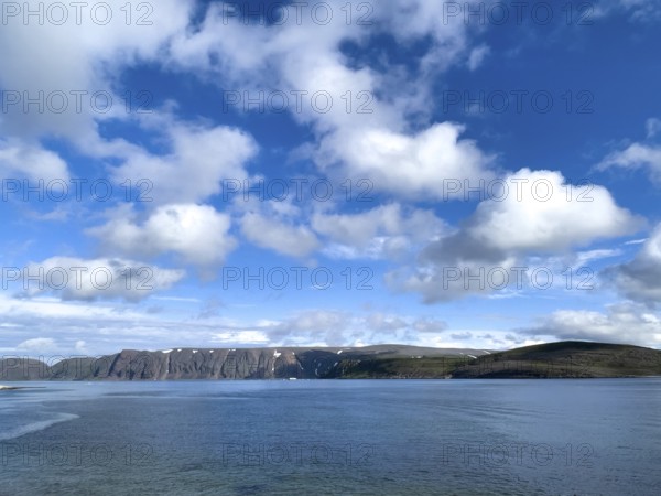 Calm sea and clear coastline under a sky with white clouds on Syltejjord on the Varanger Peninsula