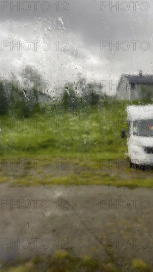 Looking through the rainy glass of a window, rain dripping along the window, cloudy sky, motorhome
