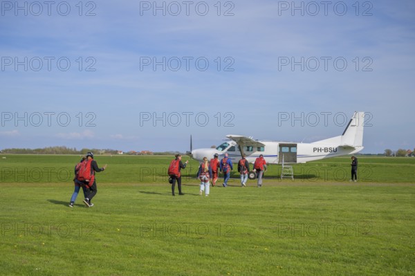 People with parachute equipment in front of a small plane on a green field, taking off for a tandem