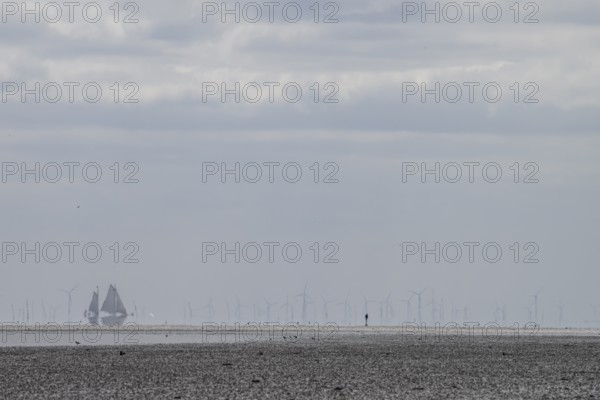 Lonely mudflats scene with wind turbines and sailing ships in the distance, grey landscape with