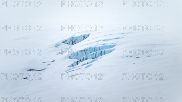 Smooth white snowy area on the glacier broken by crevasses with blue rugged glacial ice, detail,