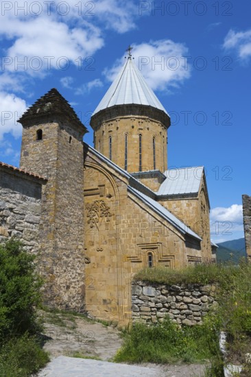 Medieval stone church with a distinctive brick tower and lush surroundings under a blue sky,