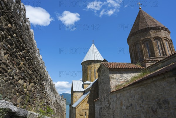 Historic monastery complex with brick towers and a surrounding stone wall under a blue sky, Ananuri