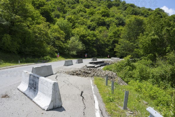A damaged road with concrete barriers surrounded by dense green forest, road near Naduknari,