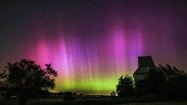Colourful aurora above the EXPO observatory in magenta and shades of green in front of a starry