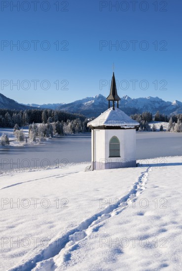 Snowy chapel against a mountain backdrop under clear blue sky with traces in the snow,