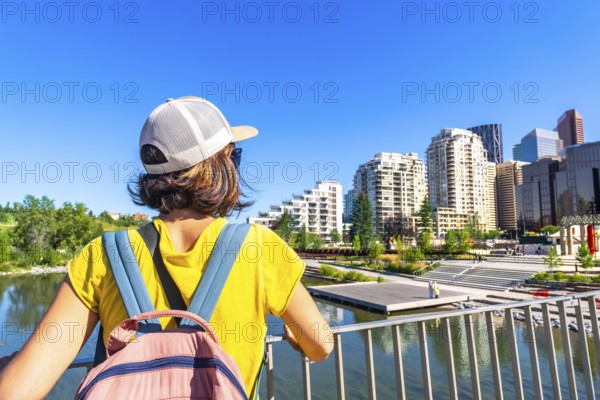Tourist with a backpack is enjoying the cityscape of calgary, alberta, from a bridge, taking in the