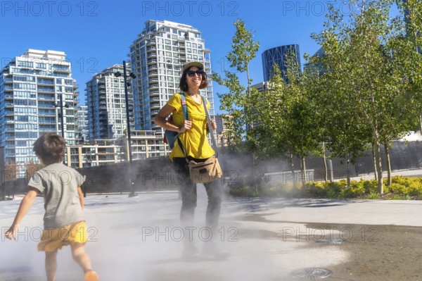 Tourist in a yellow shirt and backpack smiling while child runs through a refreshing misting system
