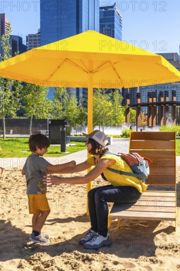 Mother and son enjoying a sunny day, playing together in a sandy urban park under a vibrant yellow