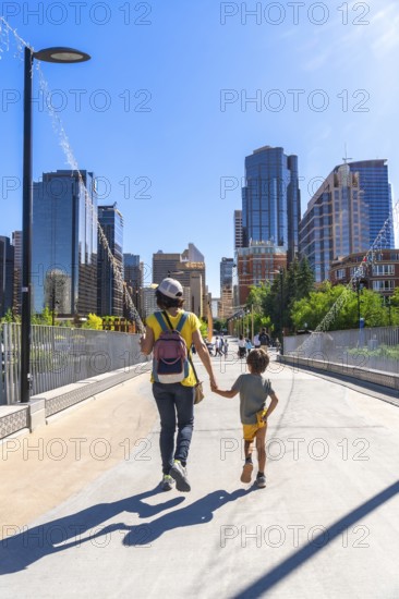 Mother and son enjoying a sunny day walking on a bridge in calgary city center, with skyscrapers