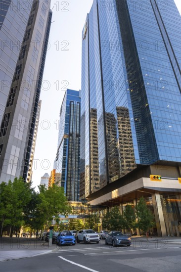 Glass skyscrapers reflecting surrounding buildings rise high above a street with cars passing by in