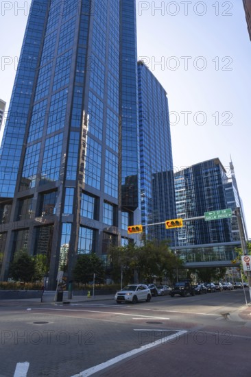 Cars navigating a busy street lined with modern skyscrapers, reflecting the vibrant blue sky in