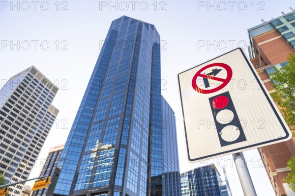 Low angle view of a no right turn sign and traffic light against towering modern skyscrapers in