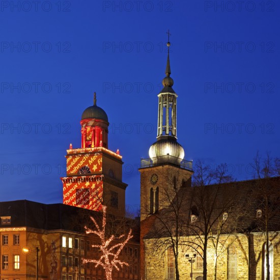 The Christmassy illuminated town hall tower and the illuminated church tower of St. John's Church