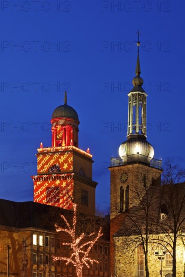 The Christmassy illuminated town hall tower and the illuminated church tower of St. John's Church