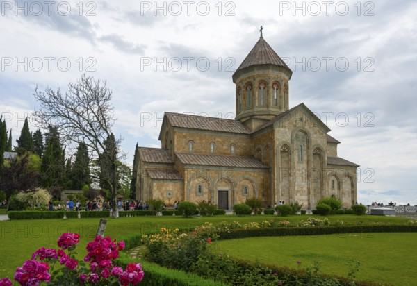 A historic church surrounded by a well-kept garden and blooming flowers under cloudy sky, Bodbe
