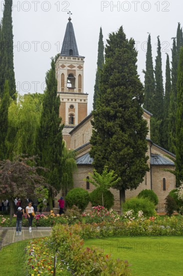 A tall church tower surrounded by blooming gardens and tall trees on a cloudy day, Bodbe monastery,