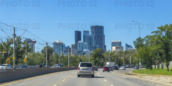 Vehicles are driving on a highway with the calgary skyline, featuring modern skyscrapers and lush