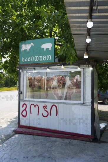 A small stand with meat presentation and signs, surrounded by green trees, butcher, small, mobile