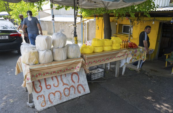 Market stand with various types of cheese and products under trees at a busy market selling cheese,