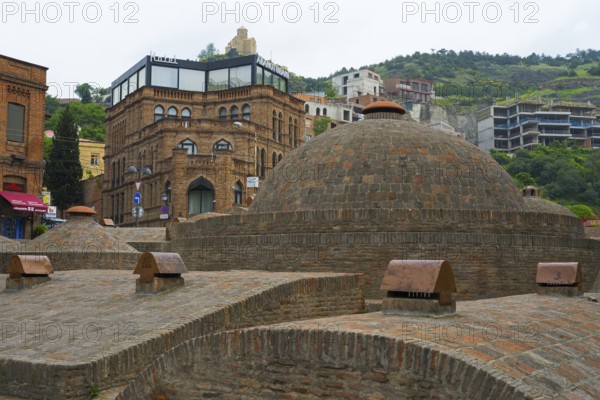 Historic brick buildings and urban baths in front of green hills, sulfur baths, Abanotubani spa