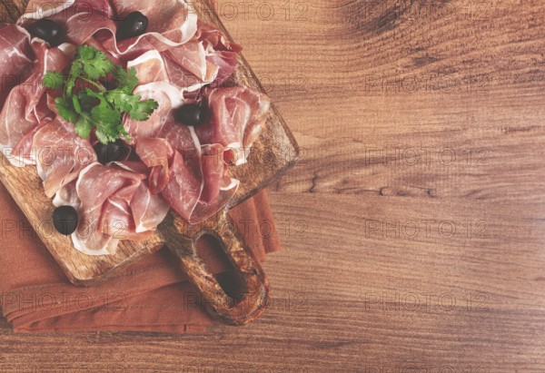 Sliced prosciutto, on a cutting board, with olives and herbs, snack, breakfast, no people