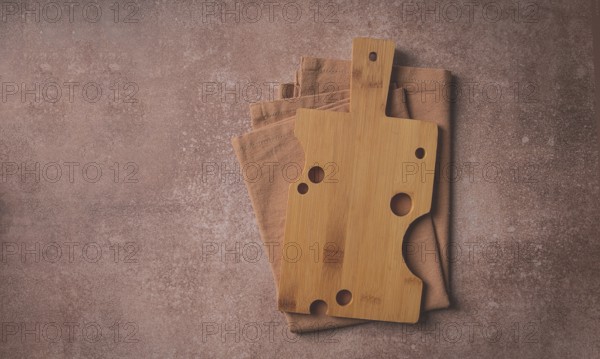 Wooden cutting board, rectangular with handle, cheese shape with holes, on a kitchen towel, top
