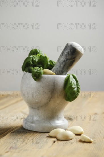 Fresh basil leaves and garlic cloves are placed in a mortar. A pestle is ready to crush the