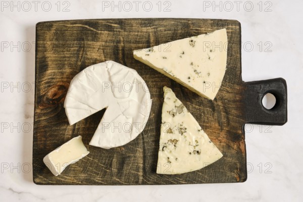 A wooden board holds pieces of cheese cut into various shapes. One piece is partially sliced,