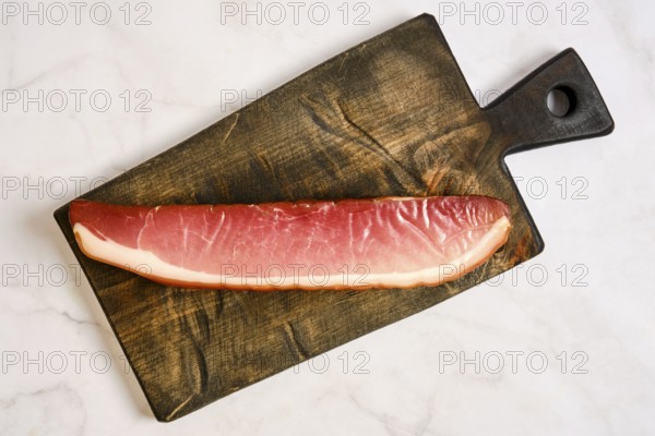A long piece of cured parma ham on a wooden cutting board. The board has a rustic design and is