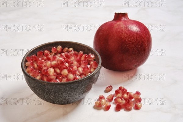 A bowl contains bright pomegranate seeds next to a whole pomegranate. The bowl is placed on a light
