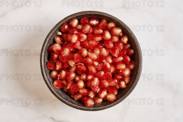 A bowl is filled with bright red pomegranate seeds. These seeds are fresh and cut from the fruit.