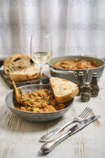 A dinner table is prepared with a bowl of food, a glass of white wine, and slices of bread. Other