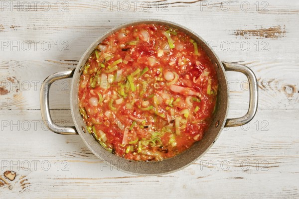 A pot filled with a mixture of chopped vegetables and tomatoes on a wooden kitchen counter. The