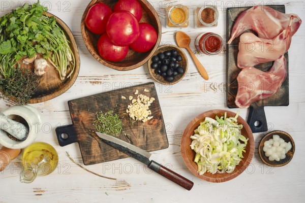 Fresh tomatoes, herbs, and meat are spread on a wooden table. There are bowls of spices and chopped