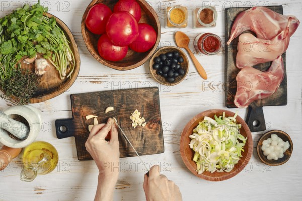 A person is chopping garlic while other ingredients are ready for cooking. Various spices sit