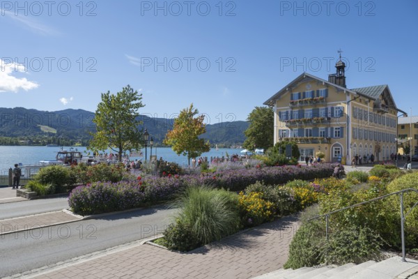 Historic town hall, tourists on the promenade on the banks of Tegernsee, flower beds in the