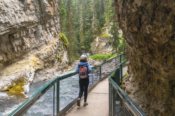 Female tourist with backpack walking on a metal catwalk enjoying the scenic view of johnston canyon