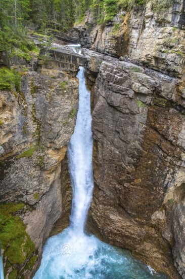 Cascading waterfall pouring into a vibrant turquoise pool amidst the rugged johnston canyon in