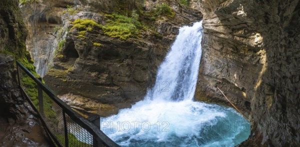 Powerful waterfall cascading into a turquoise pool in johnston canyon, surrounded by rocky cliffs